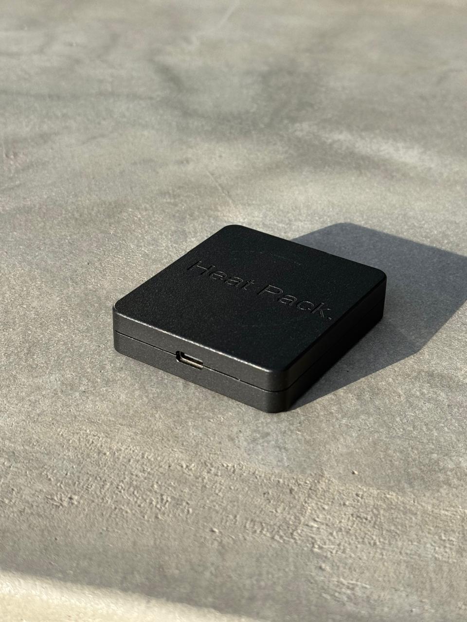 Black square device with 'Heat Pack' branding on a concrete surface